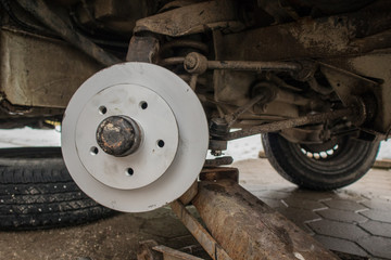 New shiny gray or silver brake disc freshly installed on an old car. Visible undercarriage of a car with rust and a new brake disc.