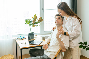 married caucasian couple happy together at home, careful wife and working husband with laptop. woman entertain, talk with him while he is at freelance work from home