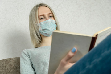 Blonde girl in medical mask reads a book, self-isolation due to covid-19