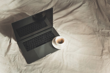 Working from home in quarantine for coronavirus. Advice for staying at home and remote working. Stay home during covid-19 pandemy. Close up white coffee cup and laptop on the bed in morning time.