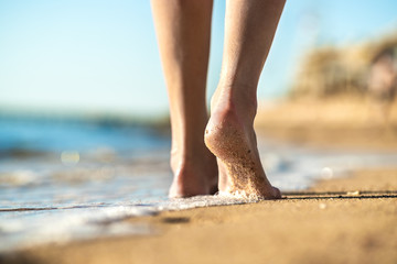 Close up of woman feet walking barefoot on sand beach in sea water. Vacation, travel and freedom...