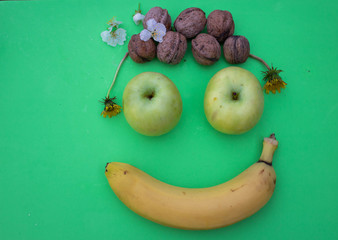 Face made of banana, apples and nuts on a green background. Fruit composition. The benefits of eating clean fruits.