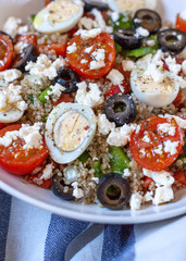 Healthy protein salad with quinoa, some vegetables and little eggs in a white bowl over a wooden tray.Closeup