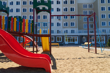 Urban residential infrastructure without people - children's playground next to a condominium. Swing, slide, stairs, multistory building. A place for children to play.