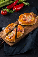 Home made small pizzas with tomatoes and cheese on wooden cutting board on dark background with wheat spikes. Healthy proper food preparation, copy space