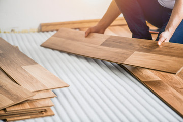 Worker hands installing timber laminate floor in modern house. Wooden floors renovation