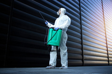 Shot of exterminator person in white chemical protection suit doing disinfection and pest control...