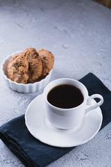 White cup of coffee with oatmeal cookies and coffee maker, breakfast concept, selective focus