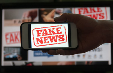 Woman holding a smartphone with fake news in front of the monitor with fake news. Blurred background