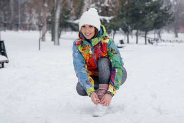 Fototapeta na wymiar A young athletic girl ties her shoes on a frosty and snowy day. Fitness, running