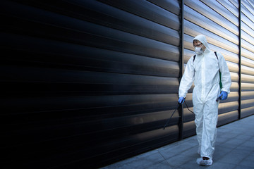 Shot of exterminator person in white chemical protection suit doing disinfection and pest control...
