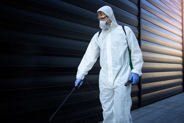 Shot of male person in white chemical protection suit doing disinfection of public areas to stop...