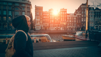 Cute young woman walks along water canal in Amsterdam at sunset sunlight, Netherlands. European...