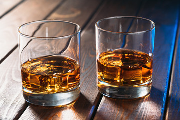 Glasses with whiskey or other alcohol drink on vintage wooden table, close up.