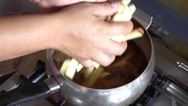 pouring several raw smashed potatoes into the pot with boiling oil