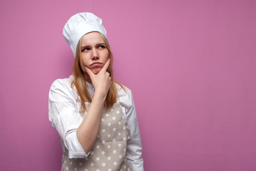 thoughtful beautiful girl cook in kitchen clothes thinks over an idea on a pink background, a woman housewife dreams and looks at a place for text