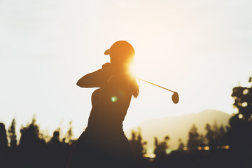 Silhouette of  young professional female golf player hit sweeping and keep golf course doing golf swing,she does exercise for relax time