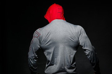 Fototapeta na wymiar A sporty guy stands in the Studio against a dark background in a hood. Sports, beauty