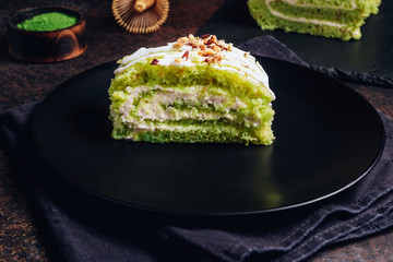 Green matcha cake rolls on black plate on dark background. Selective focus