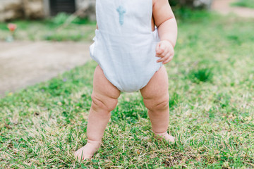 Close-up of chunky baby thighs and a boy wearing a cross medallion on his tunic. 