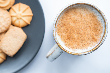 Milk in a cup with cinnamon and danish cookies in background. Top view.