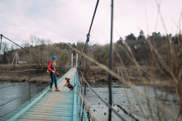 A woman walks with a dog over the river on a suspension bridge