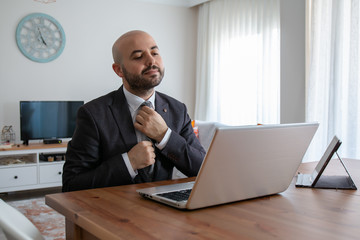 Confident man with young beard who straightens his tie and top while waiting for a job interview with a business leptop at home