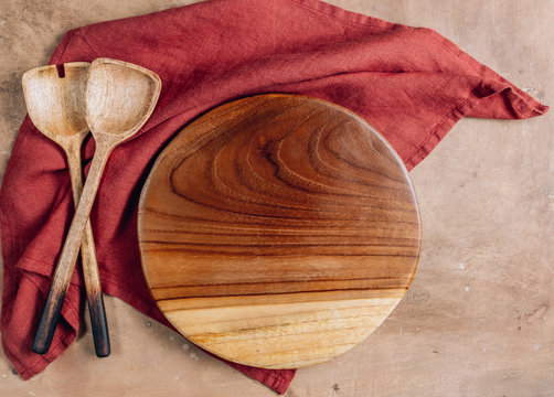 Wooden Cutting Board Over Towel With Utensils On Beige Rustic Kitchen Table. Space For Your Recipe Or Menu. Top View.