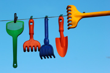 Plastic toy rakes and shovels on a clothing line against blue sky background