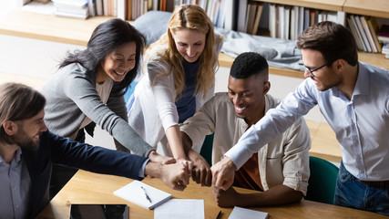 Overjoyed multiethnic businesspeople join fists motivated for shared success goal achievement at...