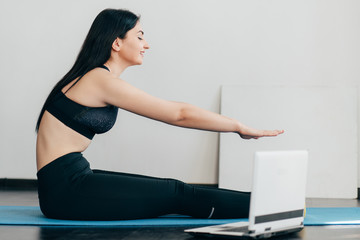 Fototapeta premium Home training,sport, online fitness class. Young fit woman doing stretching exercise on mat looking video guide on laptop
