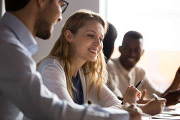 Smiling diverse multiethnic businesspeople sit in row talk discuss ideas at team briefing in office, happy multiracial colleagues speak brainstorm at group meeting in boardroom, collaboration concept