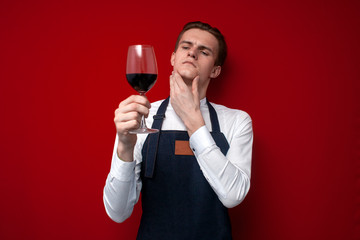 professional thoughtful sommelier holds a glass of red wine and thinks against a red background, the guy the waiter looks at the wine