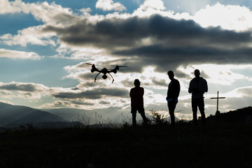 Fototapeta na wymiar Jovenes volando un dron en un contraluz nublado al amanecer