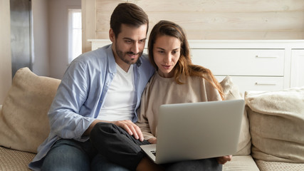 Young affectionate man cuddling mixed race girlfriend, watching funny movie in comfortable living...