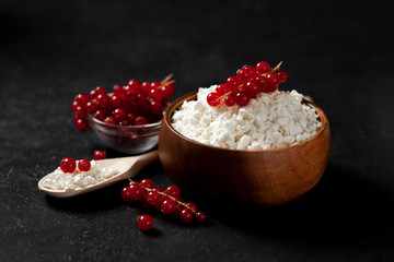 homemade cottage cheese with currants in a wooden plate against a dark background, a healthy milk breakfast with berries on a black table