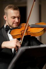 young caucasian handsome guy play violin, talented musician perform music with the use of classical instrument, wearing elegant formal suit, before concert or performance