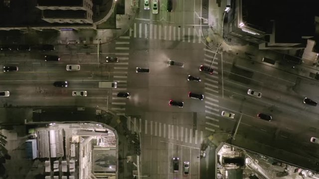 AERIAL: Overhead View on Intersection Street with big Construction Site and Holes in Ground at Night with Glowing Streets and City Car Traffic Lights 