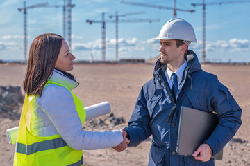 a Builder and a real estate agent shake hands in front of a building under construction