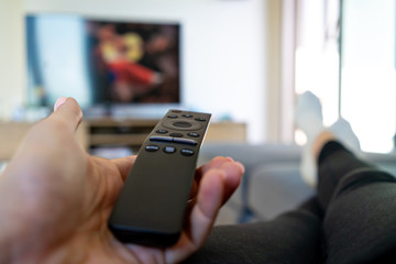 Watching TV, hand holding remote controller in front of big television