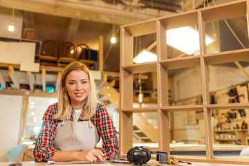 good-looking caucasian carpenter woman looking at camera, awesome lady enjoy being woodworker, sit on desk next to handicraft