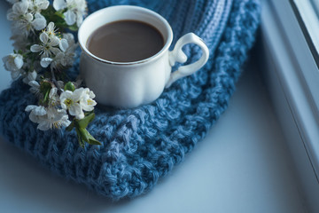 The composition consists of a cup of coffee with milk, a tweed of flowers and a scarf on the window