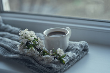 The composition consists of a cup of coffee with milk, a tweed of flowers and a scarf on the window