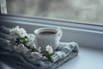 The composition consists of a cup of coffee with milk, a tweed of flowers and a scarf on the window