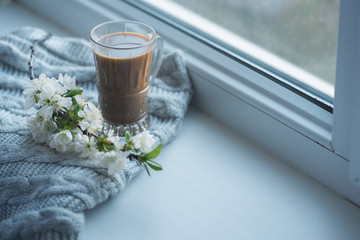 The composition consists of a cup of coffee with milk, a tweed of flowers and a scarf on the window