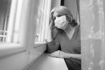 Woman with headache looking through the window wearing surgical mask, covid19 quarantine 