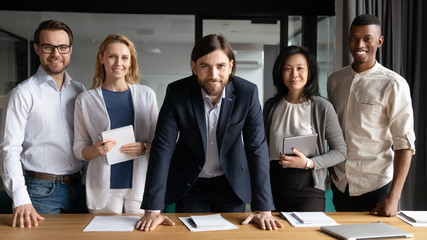 Group portrait of diverse multiracial businesspeople stand together look at camera posing in office boardroom, happy motivated multiethnic colleagues show unity team support, cooperation concept