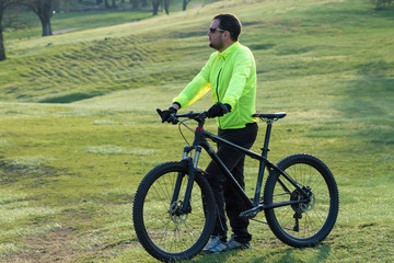 Fototapeta premium Cyclist in pants and green jacket on a modern carbon hardtail bike with an air suspension fork. The guy on the top of the hill rides a bike.