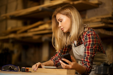 professional female carpenter with mobile phone, woman use smartphone during work, she watch marks need for work on mobile phone