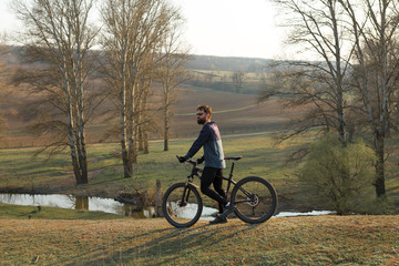 Obraz premium Cyclist in shorts and jersey on a modern carbon hardtail bike with an air suspension fork standing on a cliff against the background of fresh green spring forest